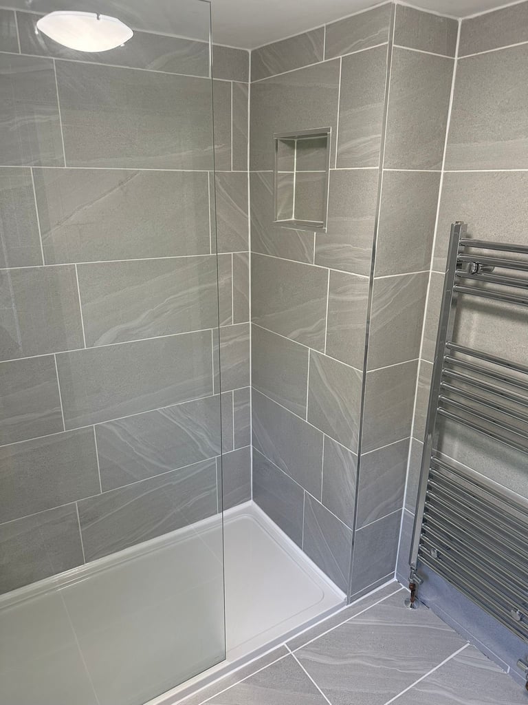 Modern bathroom shower enclosure with gray tile walls, glass door, white base, and chrome towel rack