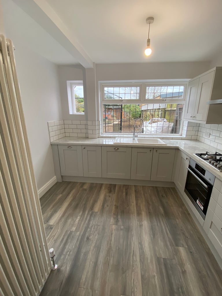 Modern kitchen with white cabinetry, subway tile backsplash, wood-look flooring, gas range, and large window overlooking garden